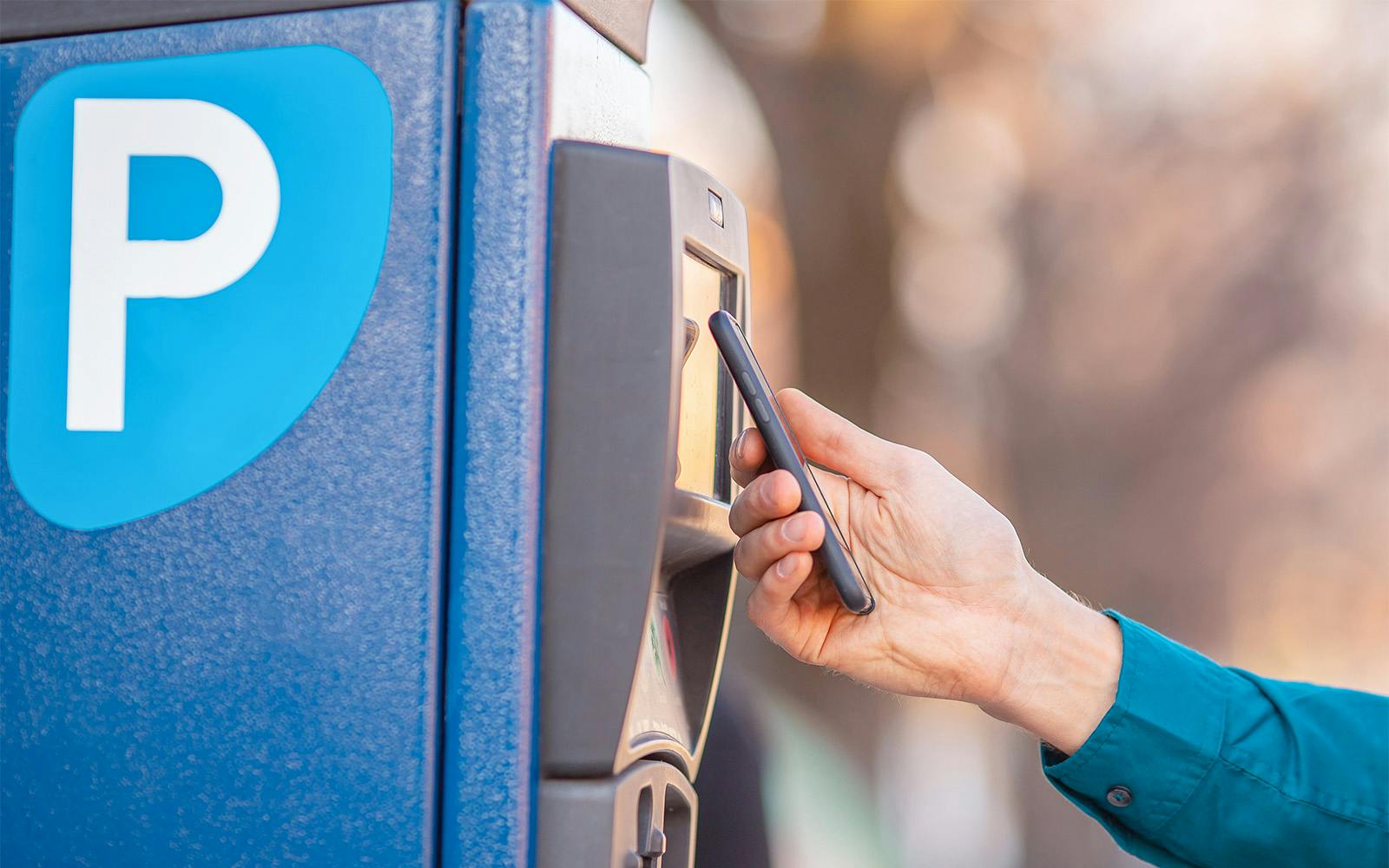 A person using a smartphone at a parking meter near Sagrada Familia.