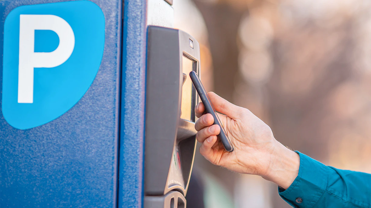 A person using a smartphone at a parking meter near Sagrada Familia.