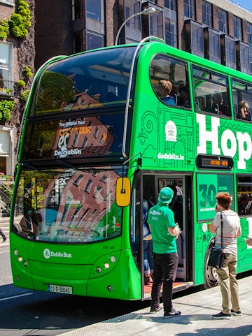 Dublin hop on hop off bus with tourists near historic city landmarks.