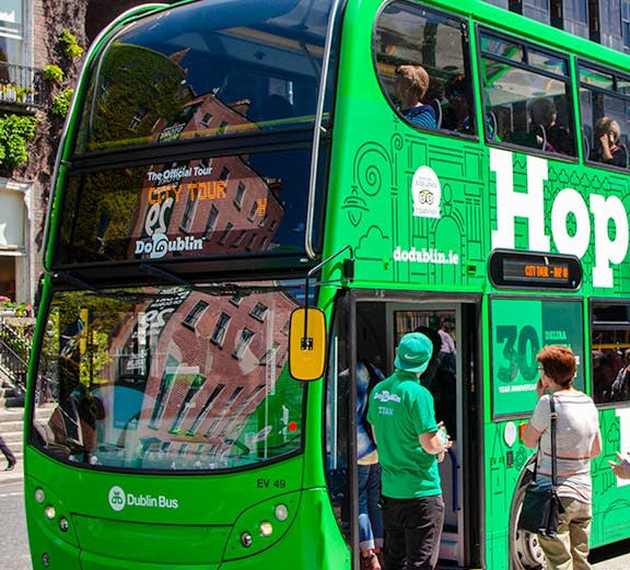 Dublin hop on hop off bus with tourists near historic city landmarks.
