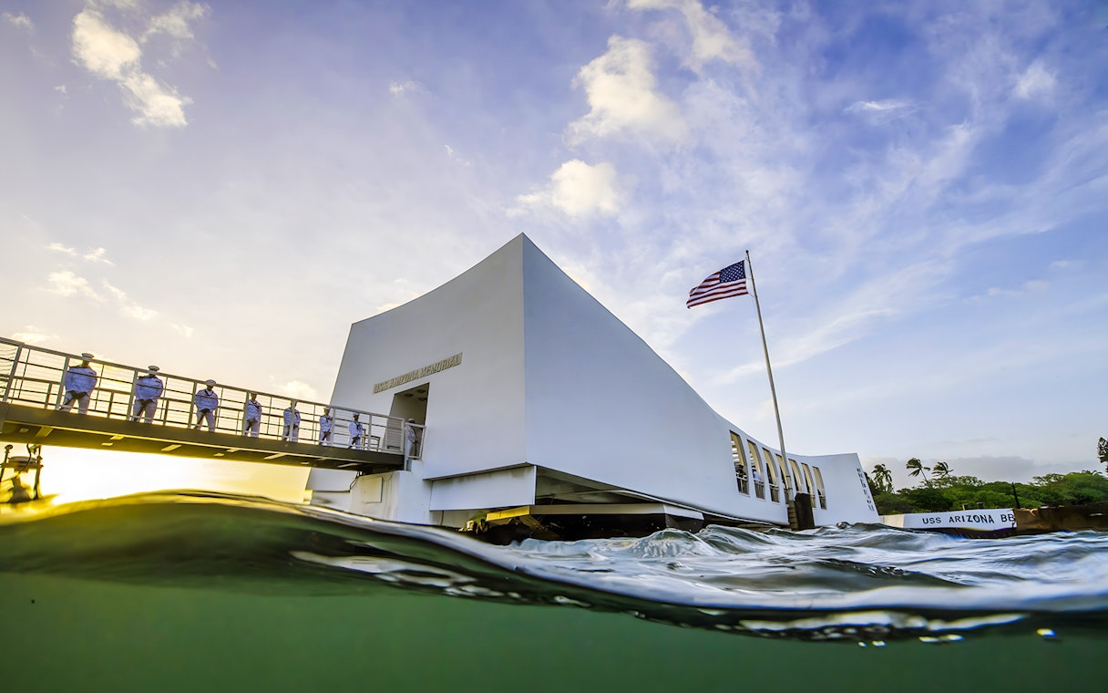 USS Arizona Memorial with American flag and visitors on the bridge in Pearl Harbor, Hawaii.