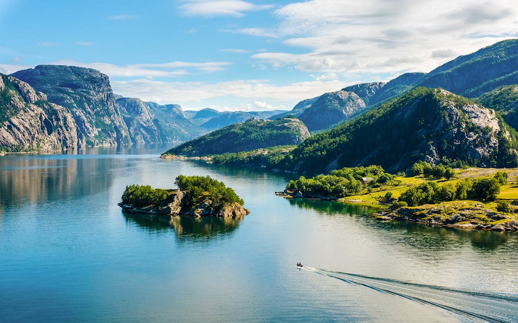Lysefjord in Norway with lush green mountains and a small boat on the water.