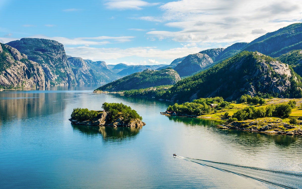 Lysefjord in Norway with lush green mountains and a small boat on the water.