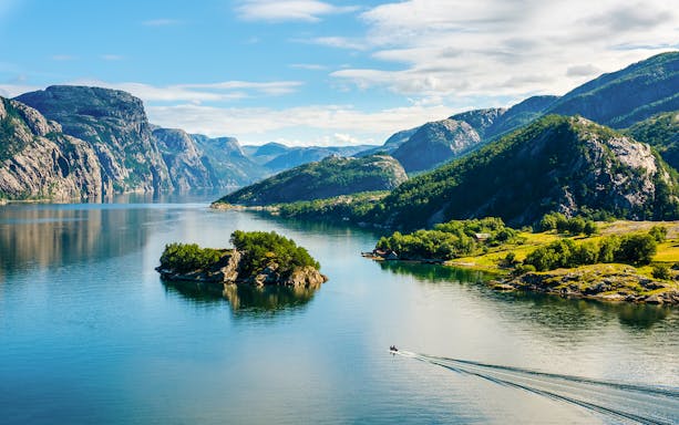 Lysefjord in Norway with lush green mountains and a small boat on the water.