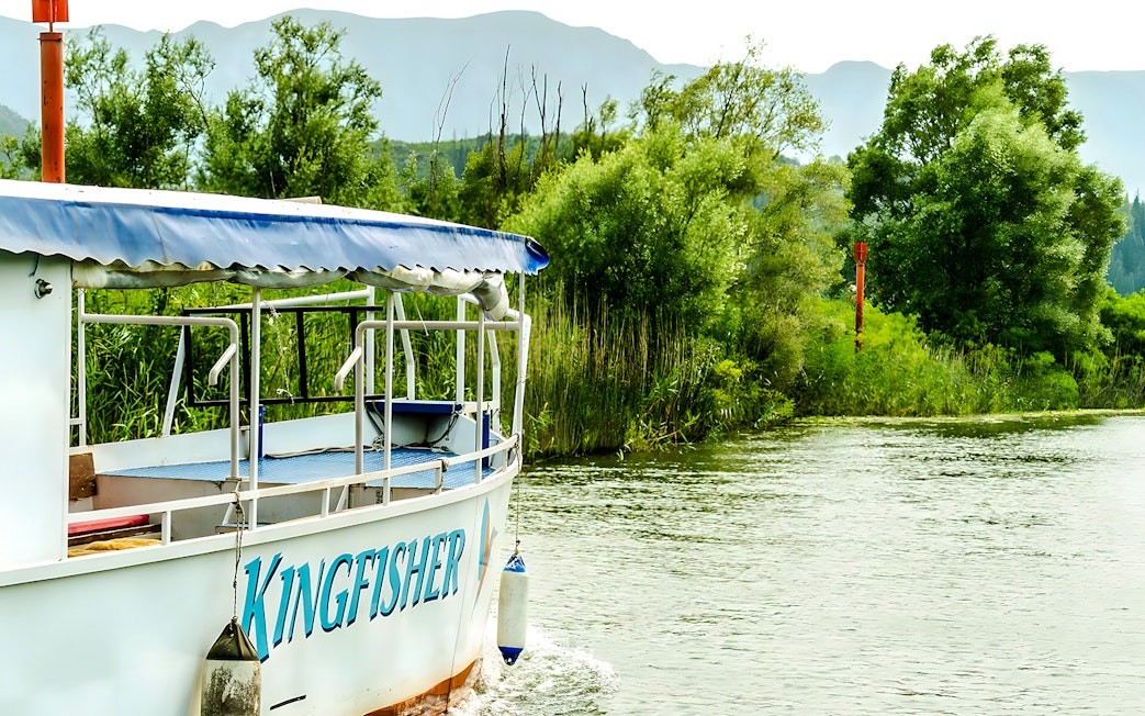 Boat named Kingfisher cruising on Lake Skadar surrounded by lush greenery.
