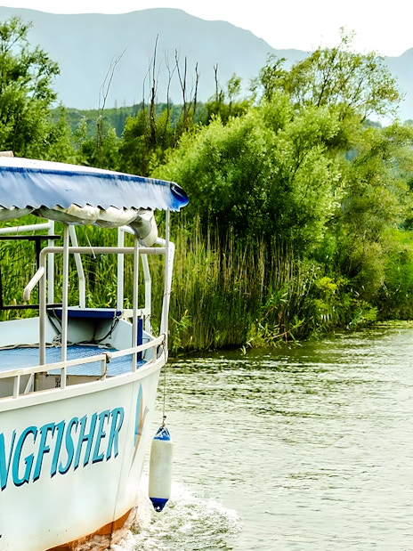 Boat named Kingfisher cruising on Lake Skadar surrounded by lush greenery.