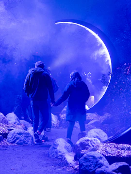 Couple walking through illuminated archway in misty garden at night.