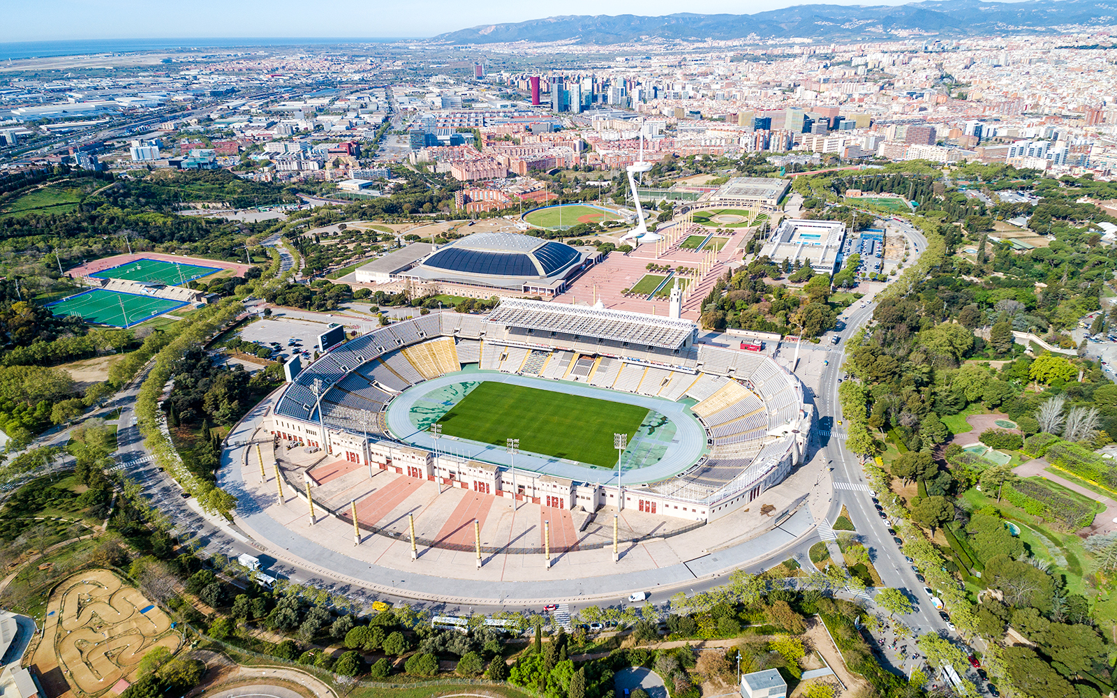 Aerial view of Montjuïc Olympic Stadium in Barcelona, Spain, surrounded by lush greenery and cityscape.