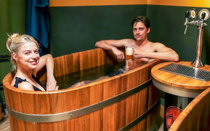 Couple enjoying beer spa in wooden tubs at Budapest's Lukács Thermal Bath.