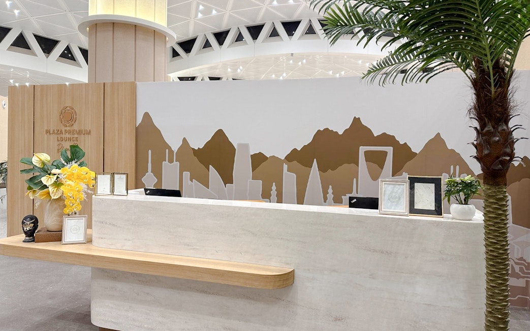 Reception desk at Plaza Premium Lounge, Riyadh, with decorative wall art and plants.