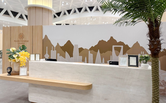 Reception desk at Plaza Premium Lounge, Riyadh, with decorative wall art and plants.