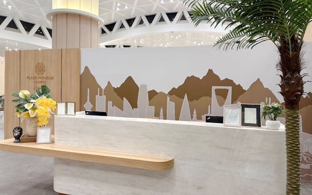 Reception desk at Plaza Premium Lounge, Riyadh, with decorative wall art and plants.