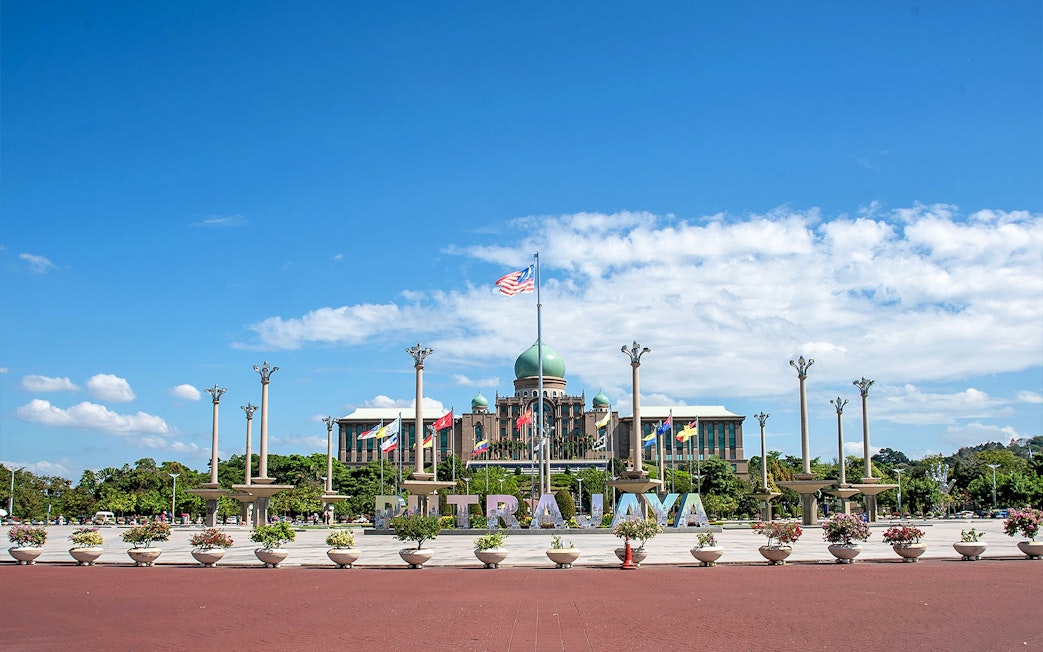 Putrajaya government complex with flags and central dome under blue sky.