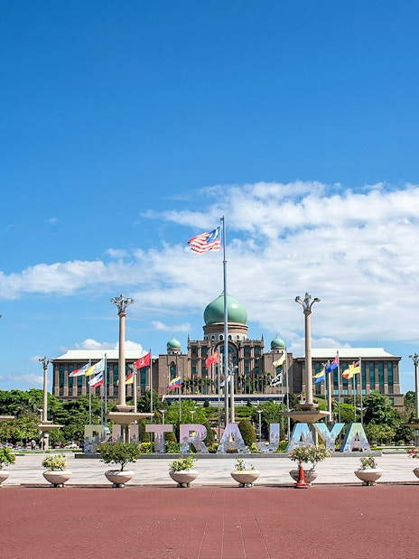 Putrajaya government complex with flags and central dome under blue sky.