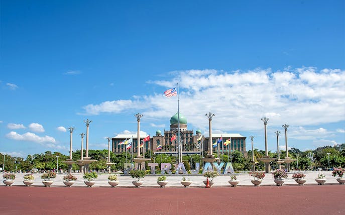 Putrajaya government complex with flags and central dome under blue sky.