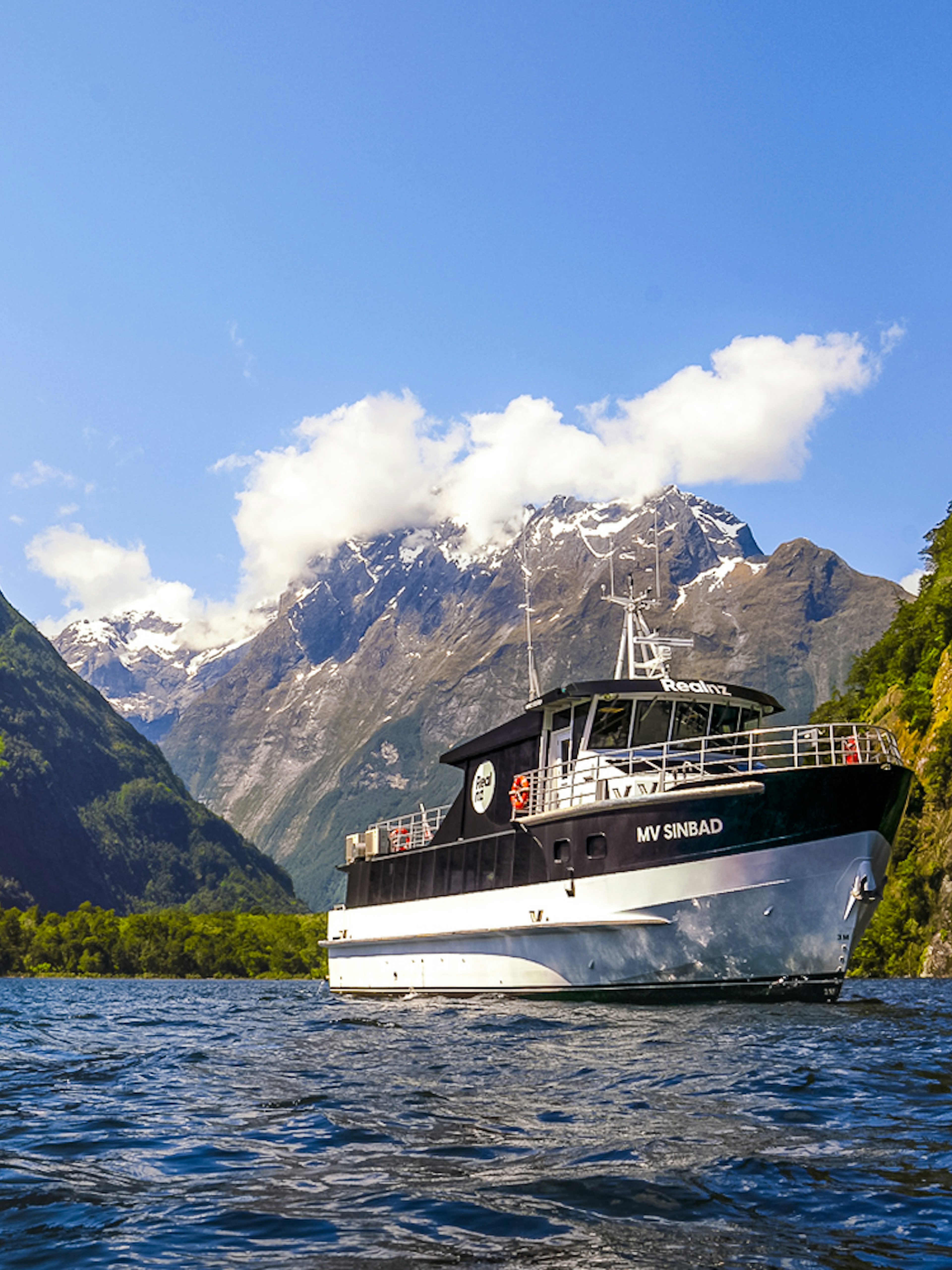 Sinbad cruise ship sailing through Milford Sound with scenic mountain backdrop.