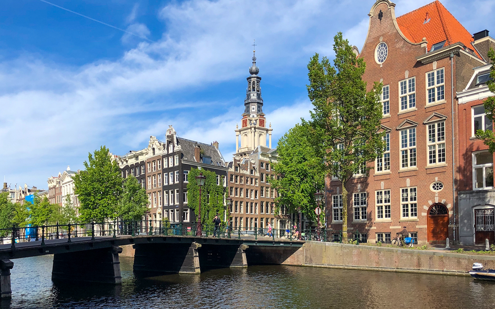 Amsterdam canal with historic buildings and bridge, ideal for a German cruise with unlimited drinks.