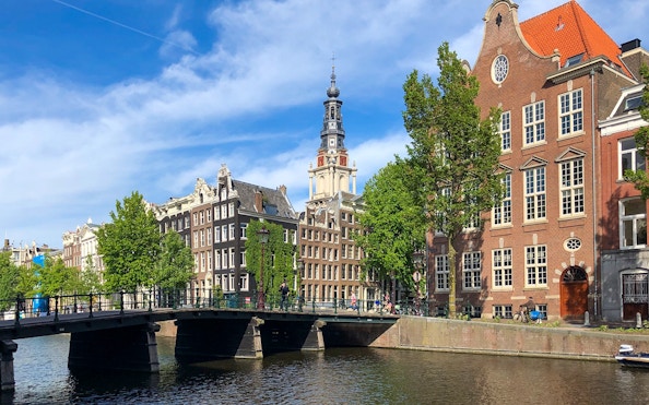 Amsterdam canal with historic buildings and bridge, ideal for a German cruise with unlimited drinks.