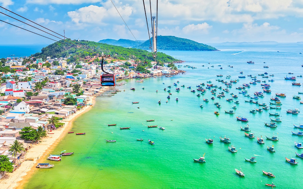 Cable car over Hon Thom Island, Phu Quoc, with colorful boats in turquoise water.