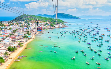 Cable car over Hon Thom Island, Phu Quoc, with colorful boats in turquoise water.