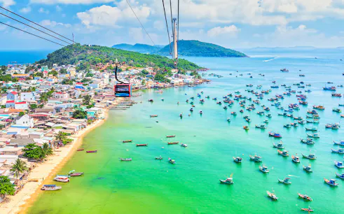 Cable car over Hon Thom Island, Phu Quoc, with colorful boats in turquoise water.