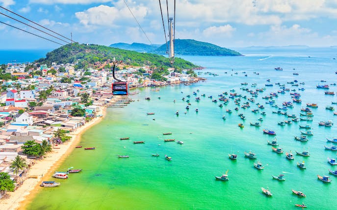 Cable car over Hon Thom Island, Phu Quoc, with colorful boats in turquoise water.