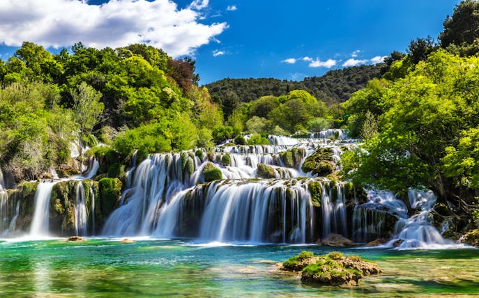 Waterfall cascading through lush greenery in Krka National Park, Croatia.