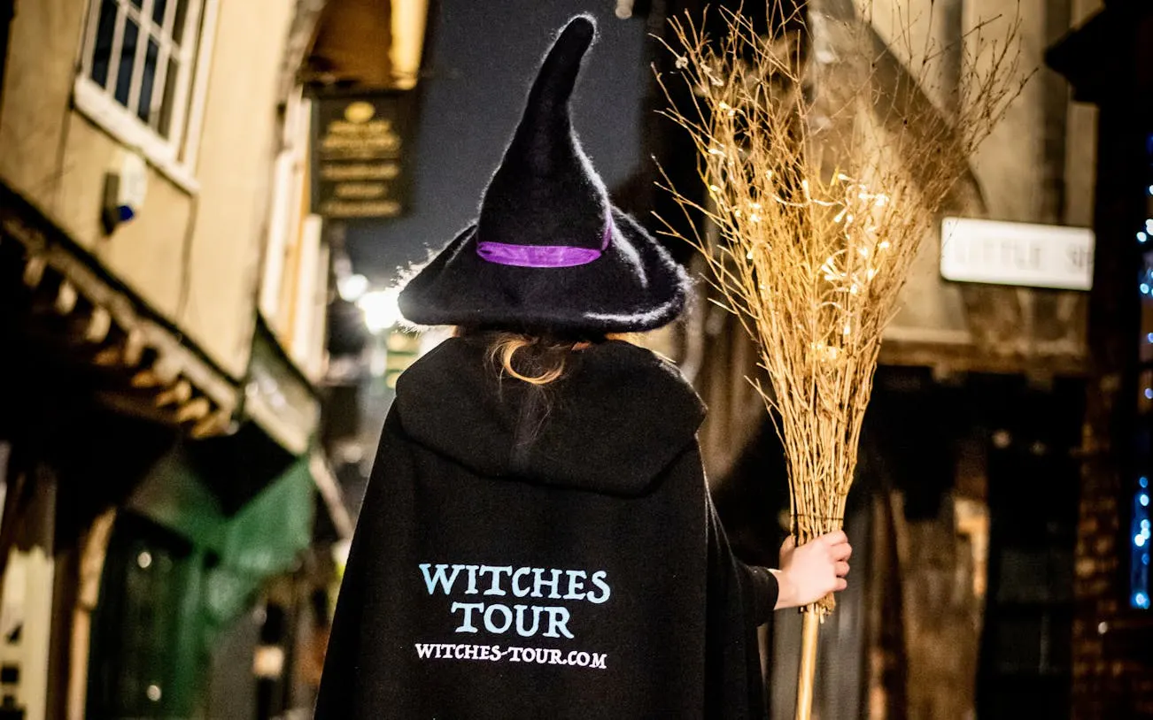 Person in witch costume holding broom on York's historic street at night.