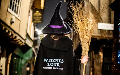 Person in witch costume holding broom on York's historic street at night.