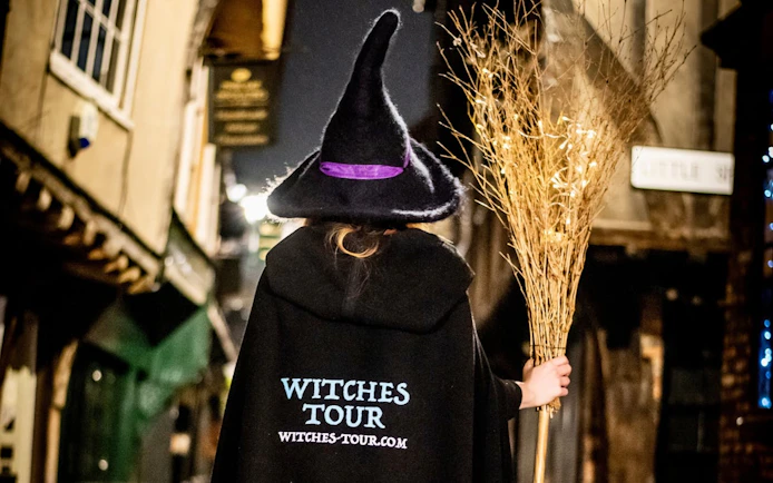 Person in witch costume holding broom on York's historic street at night.