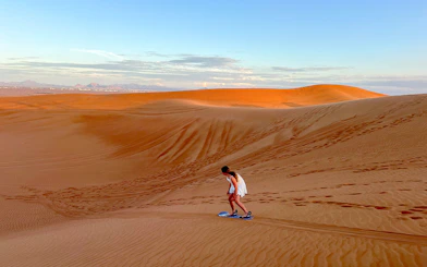 Person sandboarding on a dune in Dubai desert.