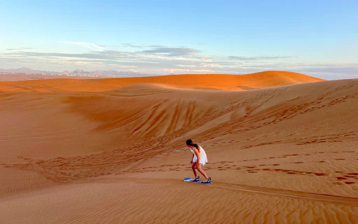 Person sandboarding on a dune in Dubai desert.
