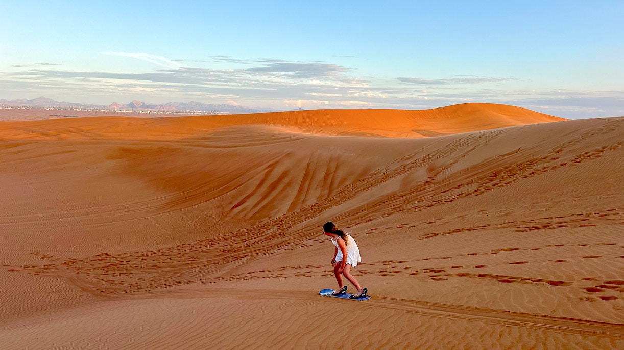 Person sandboarding on a dune in Dubai desert.