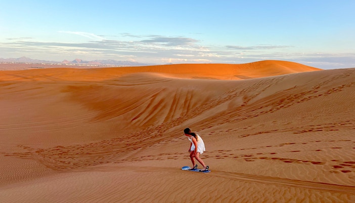 Person sandboarding on a dune in Dubai desert.