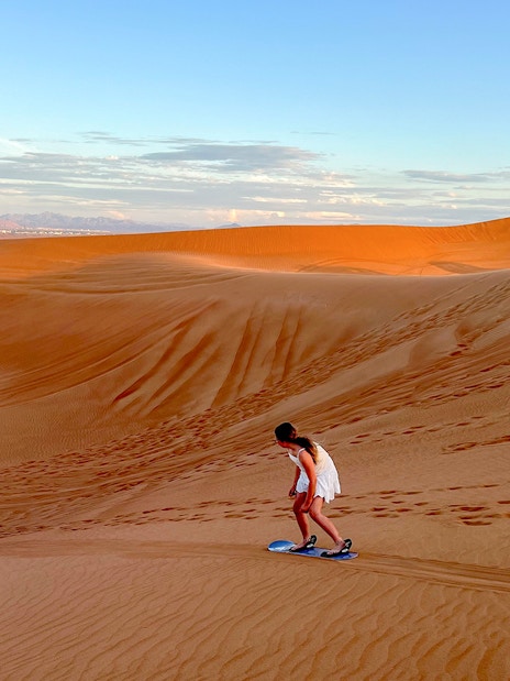 Person sandboarding on a dune in Dubai desert.