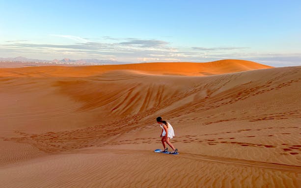 Person sandboarding on a dune in Dubai desert.