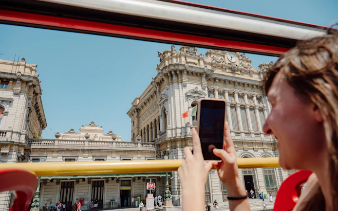 Tourist photographing historic building from Genova sightseeing bus.