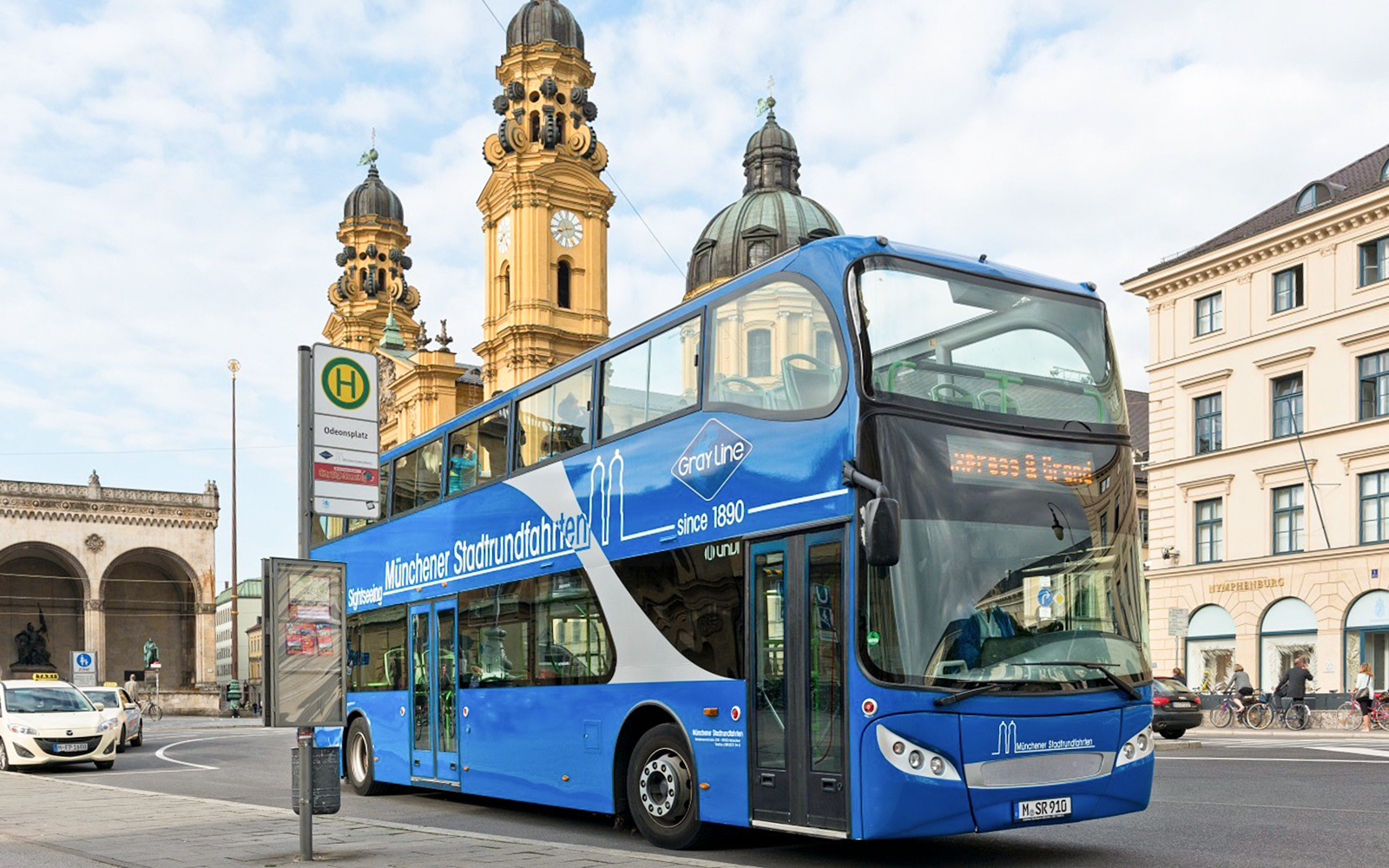 Blue double-decker tour bus at Odeonsplatz, Munich, with Theatinerkirche in the background.