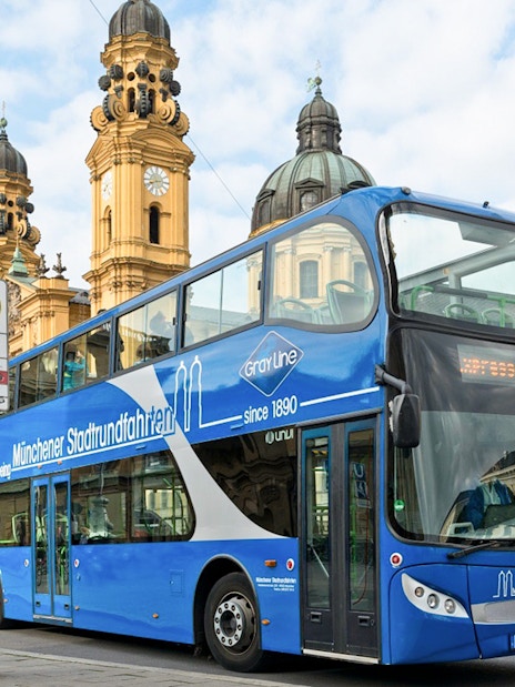 Blue double-decker tour bus at Odeonsplatz, Munich, with Theatinerkirche in the background.