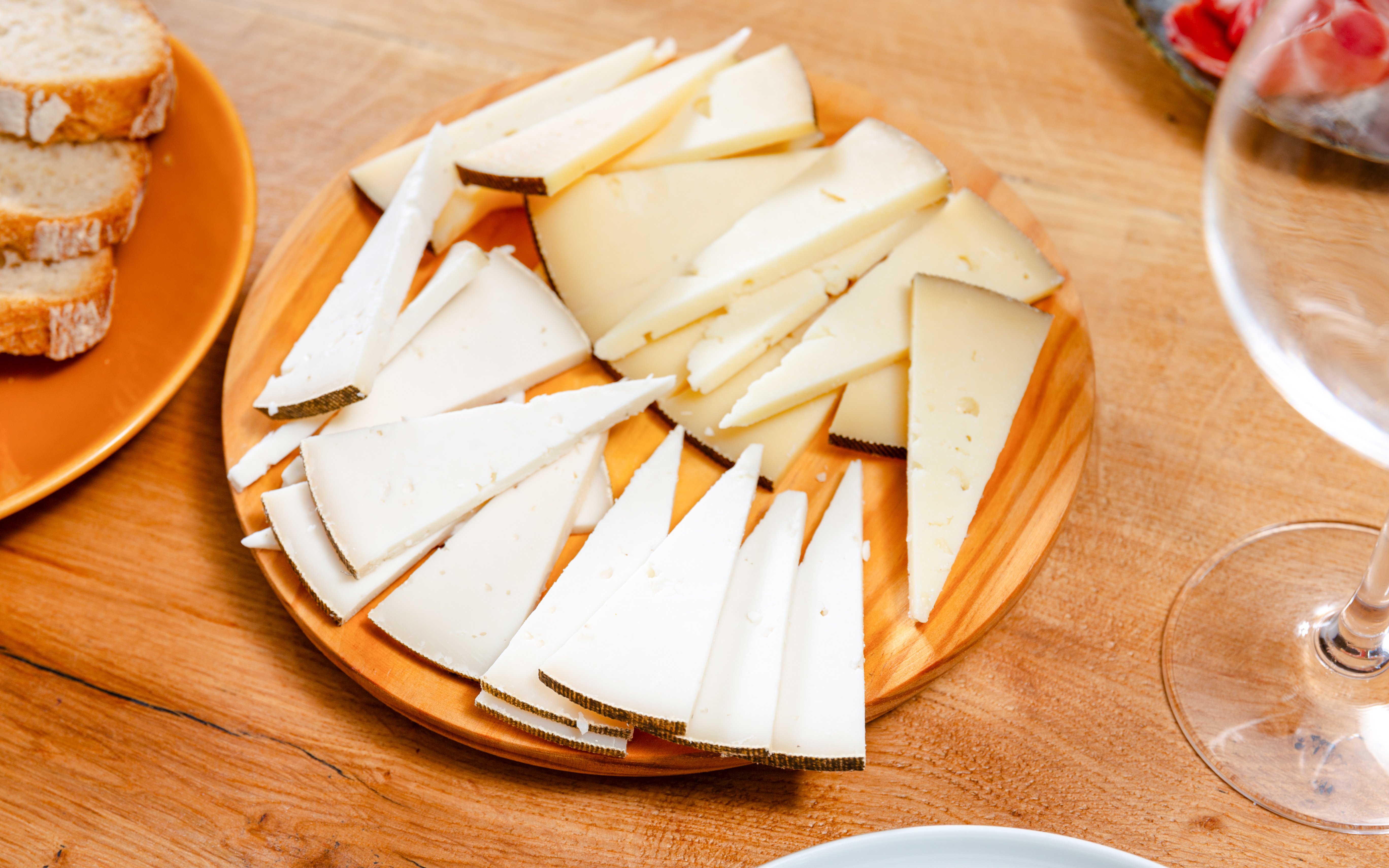 German gourmet cheese slices on a wooden platter with bread and wine nearby.