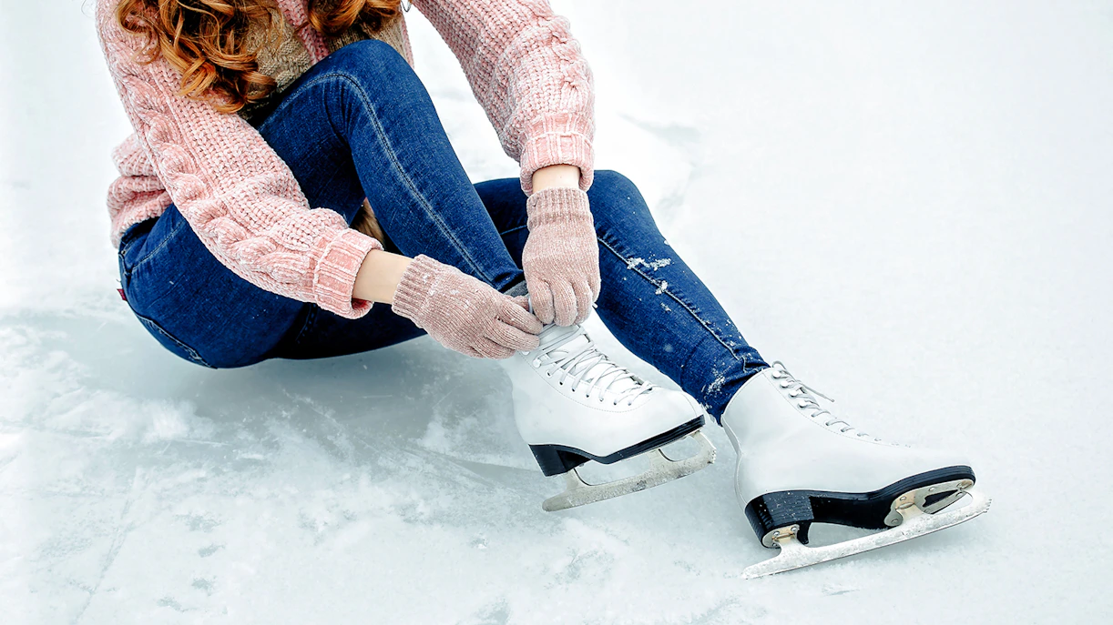 Girl tying shoelaces on ice skates on a snowy surface.