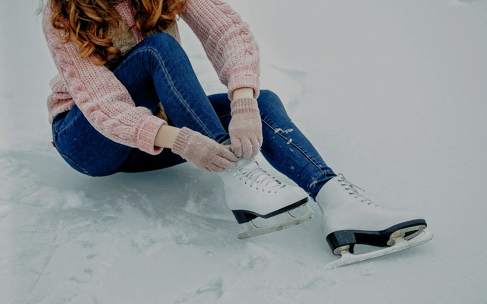 Girl tying shoelaces on ice skates on a snowy surface.
