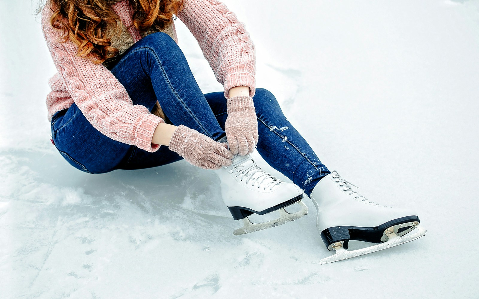 Girl tying shoelaces on ice skates on a snowy surface.