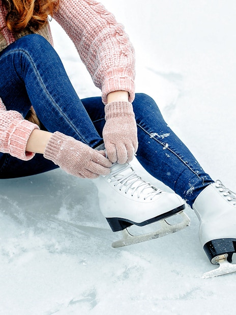 Girl tying shoelaces on ice skates on a snowy surface.