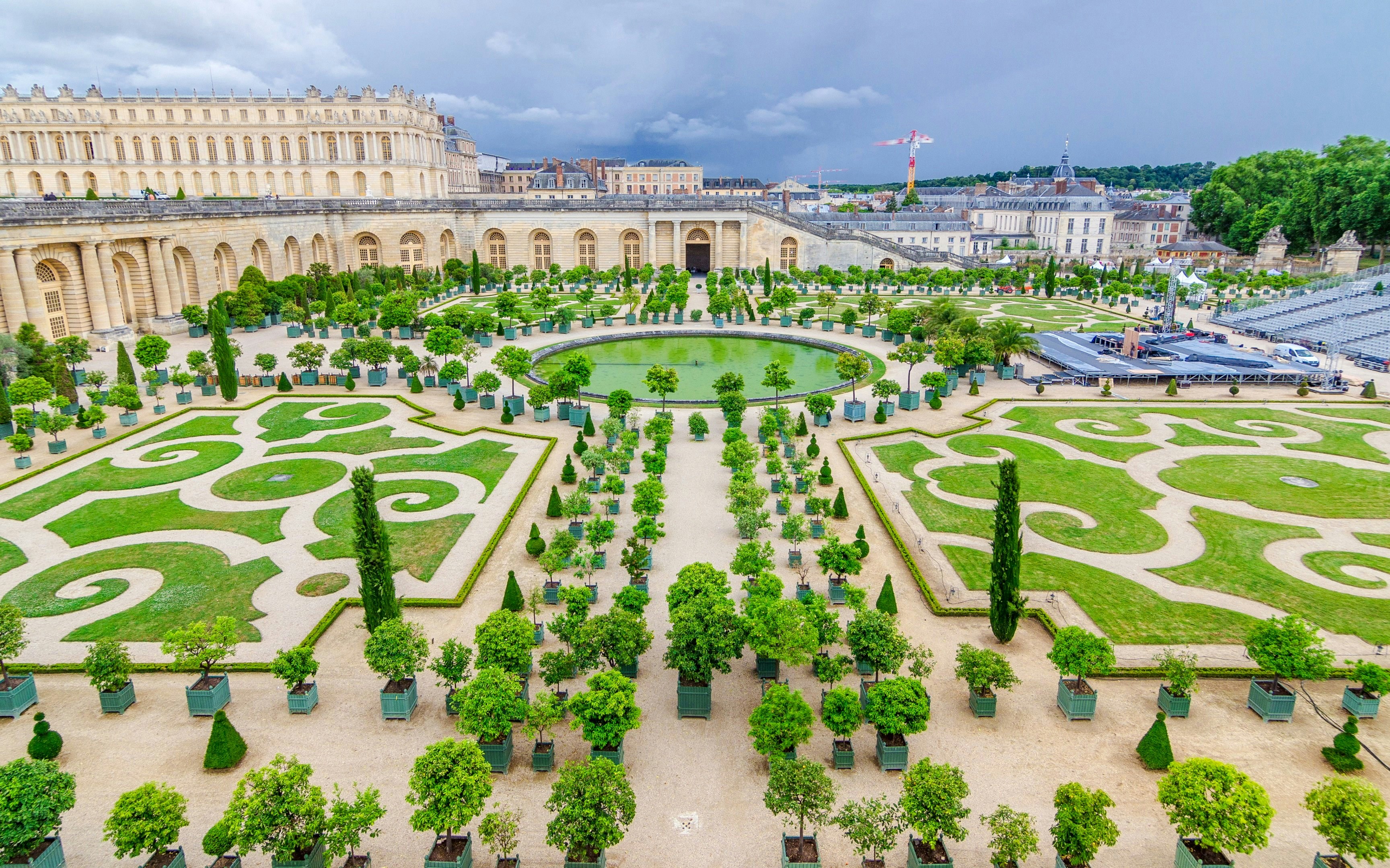 Versailles Gardens with manicured lawns, symmetrical paths, and the Palace of Versailles in the background.