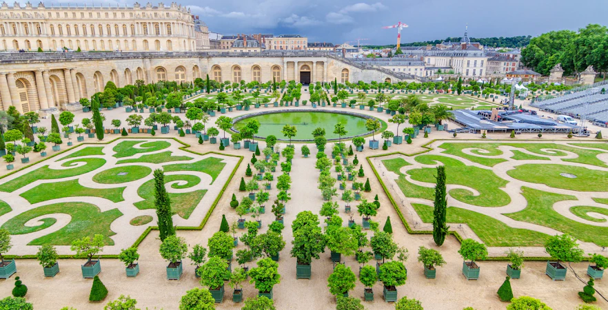 Versailles Gardens with manicured lawns, symmetrical paths, and the Palace of Versailles in the background.