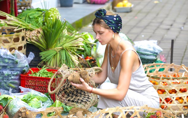 Woman selecting fresh produce at a Balinese market for Nia Balinese Cooking Class.