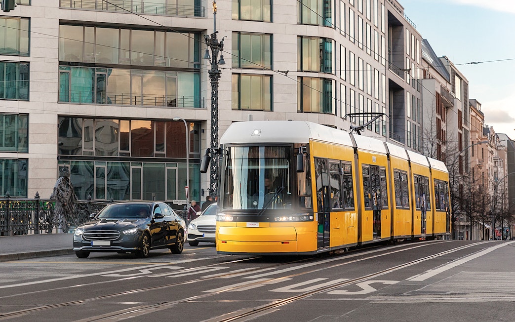 Yellow tram traveling through Berlin city street with modern buildings.