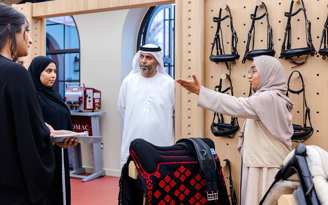 Guide explaining equestrian equipment to visitors at Abu Dhabi Royal Equestrian Arts tour.