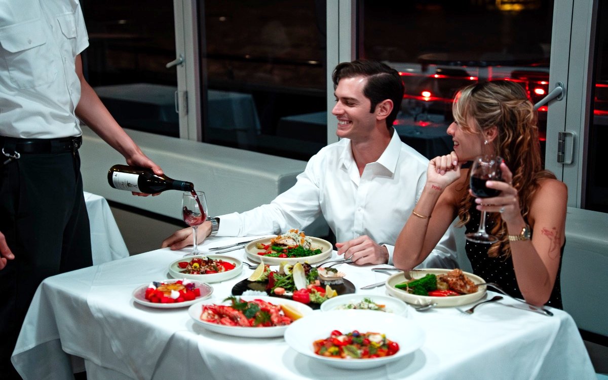 Waiter serving wine to couple on Glass Boat Dinner Cruise in Sydney.